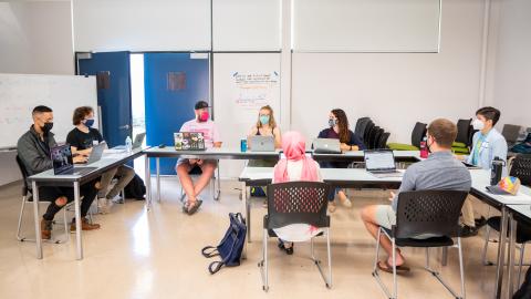 photo of a classroom and 8 people seated at tables