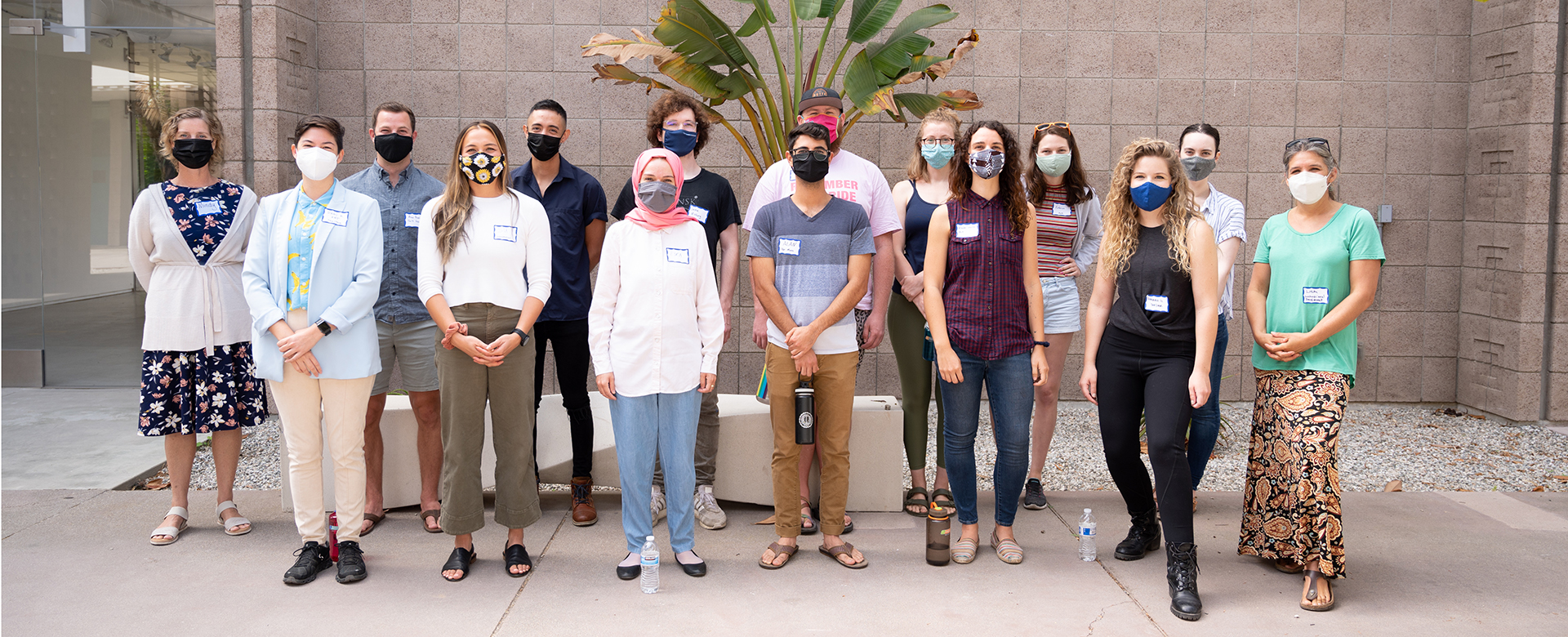 photo of a group of masked people standing outdoors in front of a brick building