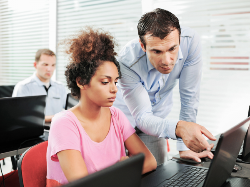 photo of person assisting another at a laptop