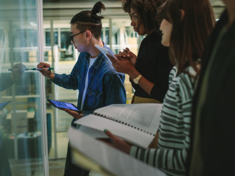 photo of three people standing at a glass board one writing on it