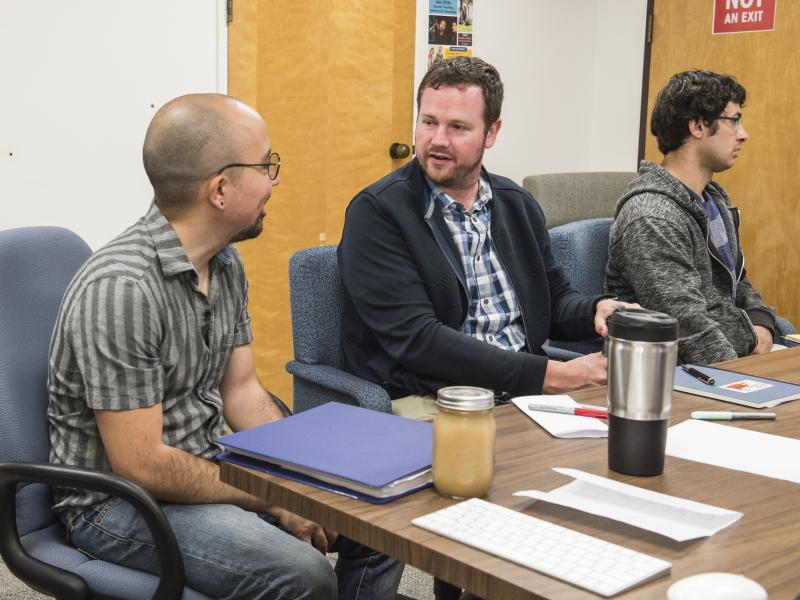 photo of three people sitting at a table two of the people are conversing