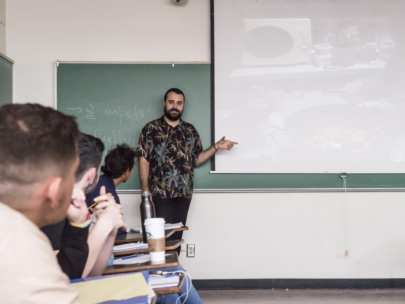 photo of person pointing to projector screen while talking with seated people