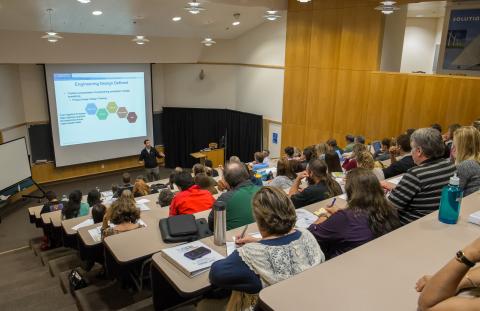 photo with an angled side view of people attending a lecture with stadium seating